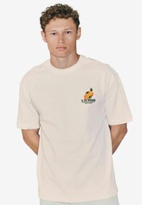 Light beige short-sleeve t-shirt made of cotton, featuring a small graphic of oranges and text on the left chest area.