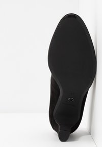 Bottine en suède noir avec un bout pointu et une semelle noire élégante. Présente un talon empilé bas et un design minimaliste. Taille 37.