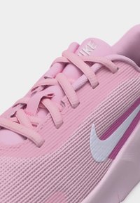 Zbliżenie na różowy sneaker Nike z teksturowaną tkaniną, różowymi sznurowadłami i białym logo Nike po boku.