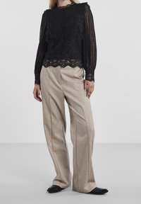 Haut en dentelle noire à manches longues avec des détails froncés et un ourlet festonné, associé à un pantalon beige à jambes larges avec une finition texturée. Chaussures noires.