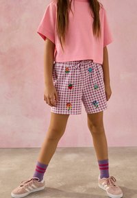 Roze korte mouwen crop top gecombineerd met paarse gingham shorts met geborduurde fruit- en bloemenontwerpen. Roze sokken en sneakers maken de look compleet.