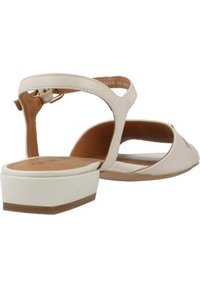 Sandali beige chiari con una sola fascia, punta aperta e un tacco basso a blocco. Parte superiore in sintetico liscio con una soletta marrone a contrasto. Fascia per la caviglia regolabile.