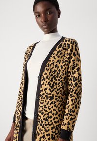 Kardigan z leopardjim vzorcem v bež in črni barvi, z V-izrezom, gumbi spredaj in rebrastimi manšetami. Gladka tekstura z drznih vzorcem.
