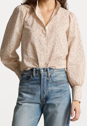 Vrouw draagt een lichtroze bloes met bloemenpatroon met opgepofte lange mouwen en lichtblauwe jeans met een hoge taille.