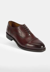 Chaussure en cuir brun à lacets avec un design à bout fleuri, présentant une texture lisse et des détails de couture subtils. La semelle en caoutchouc offre une bonne adhérence.