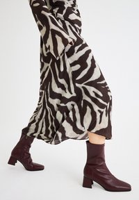 Vestido de patrón de cebra en tonos marrones y crema con mangas largas, combinado con botines burdeos de tobillo con un tacón chunky y textura suave.