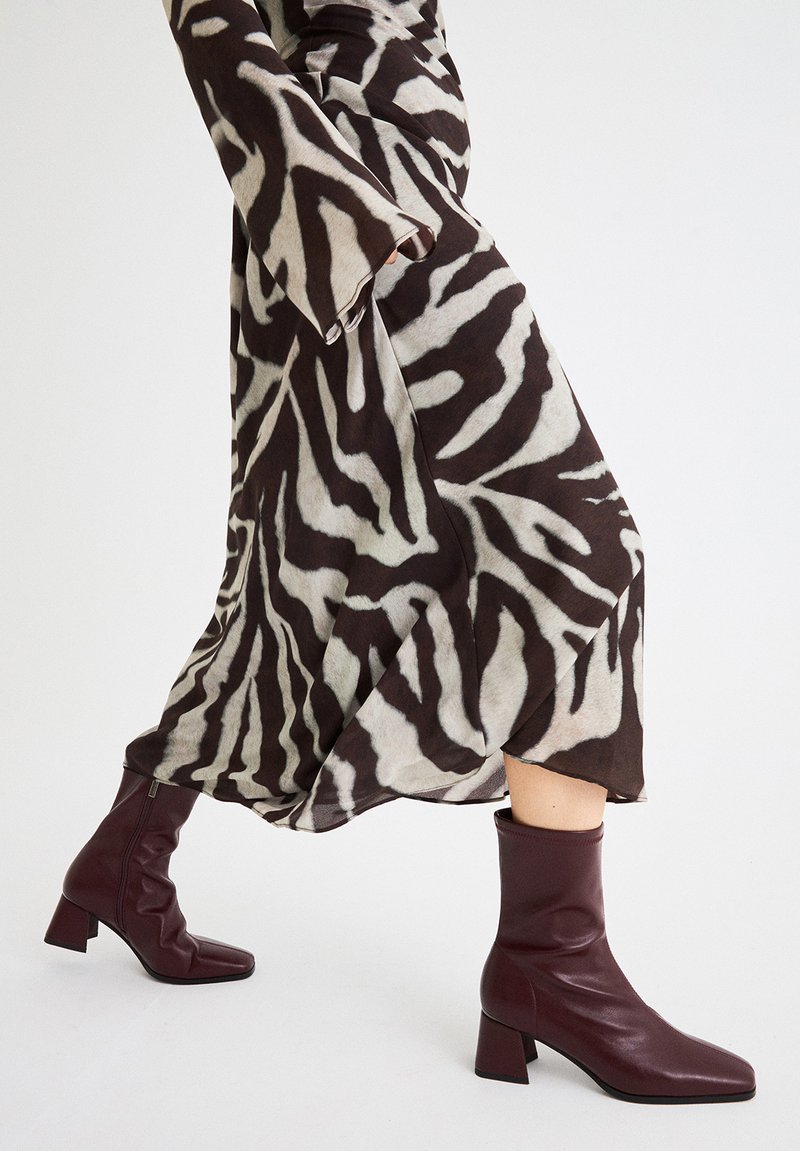Vestido de patrón de cebra en tonos marrones y crema con mangas largas, combinado con botines burdeos de tobillo con un tacón chunky y textura suave.