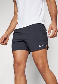 Pantalones cortos deportivos negros hechos de tela ligera. Presentan bolsillos laterales, un dobladillo dividido y un pequeño logo blanco de Nike en el frente.
