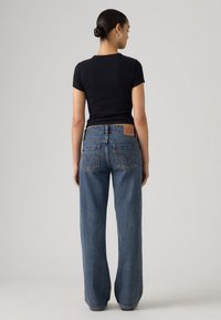 Μαύρο εφαρμοστό μπλουζάκι συνδυασμένο με φαρδιά, μεσαίου μπλε χρώματος τζιν με ψηλή μέση, με πίσω τσέπες και ταμπέλα από δέρμα σε καφέ απόχρωση.