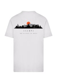 Weißes T-Shirt mit einem grafischen Druck von Bergen, Gebäuden und einer Sonne. Der Text lautet "FLIEHE UND ENTDECKE DIE WELT" in Schwarz.