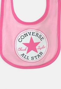 Ružičasti pamučni bib s okruglim otisnutim logotipom sa središnjom zvijezdom i tekstom "CONVERSE ALL STAR" u crnim i bijelim nijansama.