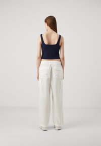 Débardeur ajusté bleu marine avec larges bretelles, associé à un pantalon cargo blanc ample dotés de poches latérales et d'une taille élastique.