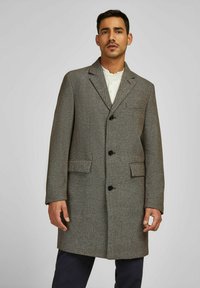 Grijze textuur wol coat met een notch-kraag, drie donkere knopen, twee voorzakken en een middellange ontwerp. Gekleed over een wit shirt.