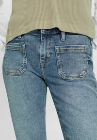 Ljusblå jeanstyp med standard femfickorsdesign, synlig sömnad och en något blekt textur. Bärs med en ljusgrön stickad topp.