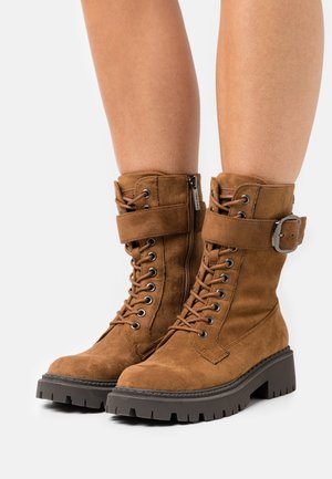 Ruske nubuk lace-up saapaat sivuvetoketjulla, solkiremmin yksityiskohdalla ja paksulla, teksturoidulla pohjalla. Varustettu metallisine silmukoineen ja ommelluilla yksityiskohdilla.