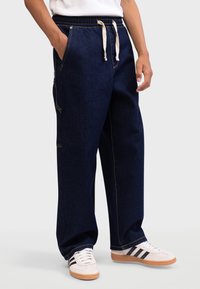 Denim pants with an elastic waistband and drawstring, featuring a dark blue color, contrast stitching, side pockets, and a relaxed fit.