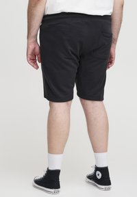 Black cotton shorts with an elastic waistband, side pockets, and a back pocket, paired with black high-top sneakers and white socks.