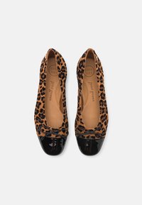 Paire de ballerines imprimé léopard avec bouts vernis noirs et petits nœuds vues de dessus sur un fond clair.