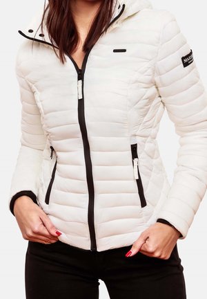 Woman wearing a white quilted jacket with black zipper details and a hood, hands on hips, paired with black pants and red nail polish.