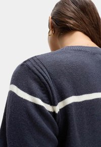 Granatowy sweter z białym poziomym paskiem, teksturowana dzianina, okrągły dekolt oraz widoczne detale szwów na ramionach.