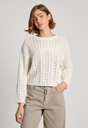 Maglione all'uncinetto color crema con scollo rotondo, maniche lunghe, design a trafori e vestibilità corta. Abbinato a pantaloni beige chiaro.