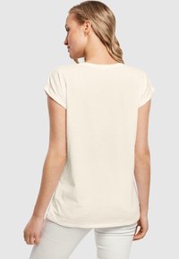 Kortærmet creme t-shirt lavet af blødt stof; afslappet pasform med op rullede ærmer og en buet kant. Minimalistisk design, ingen synlige logoer eller mønstre.