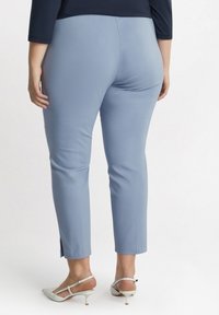 Blauwe op maat gemaakte broeken met een gladde textuur en een zijsplit aan de onderkant, gecombineerd met witte hakken, getoond vanuit de rug.