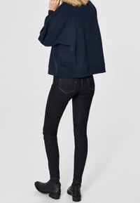 Maglione blu navy con una vestibilità comoda, abbinato a jeans neri aderenti e stivaletti neri alla caviglia. Il tessuto sembra morbido con dettagli minimi.