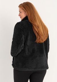 Zwarte, fluffy fleece jas met een hoge kraag, met een zachte textuur en een relaxte pasvorm. Geen zichtbare hardware of patronen.