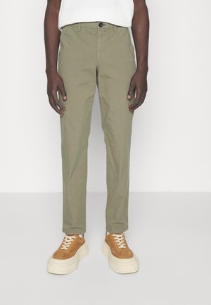 Olive green cotton chinos with a straight fit, featuring a button closure and side pockets, paired with brown sneakers on a textured sole.