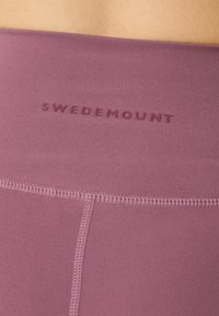 Lilla træningstøjslinning med præget "SWEDEMOUNT" logo. Glat tekstur og synlige syning detaljer. Tætsiddende design.
