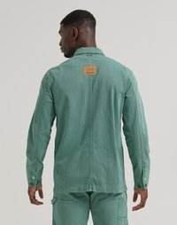 Veste en velours côtelé vert avec un motif à rayures verticales, dotée d'un label en cuir beige, de poignets boutonnés et d'un col classique.