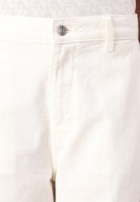 White denim pants featuring a metal button closure, belt loops, and subtle texture. The fabric appears sturdy with a classic cut.