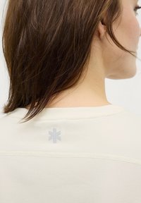 Lichtbeige shirt met een ronde halslijn, met een subtiele logo-detail op de achterkant, gemaakt van zachte, gladde stof.
