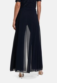 Granatowa maxi spódnica wykonana z lekkiego, przezroczystego materiału. Posiada boczne rozcięcia i gładką talię, zestawiona z obuwiem na obcasie.