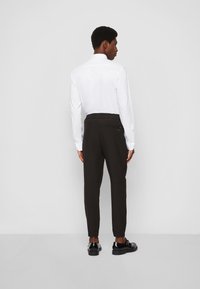 Čierne zúžené nohavice s elastickým pásom, slim fit a manžetami na členkoch, v kombinácii s bielou košeľou na gombíky a čiernymi topánkami.