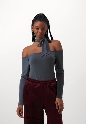 Sivi off-shoulder top dugih rukava s detaljem čvora oko vrata, u kombinaciji s burgundijskim hlačama mekanog tekstura koje imaju elastičnu traku u struku.