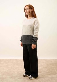 Sweter robiony na drutach w poziome paski w jasnoszarym i ciemnoszarym kolorze, z prążkowanymi mankietami; zestawiony z luźnymi czarnymi spodniami i sportowymi butami.