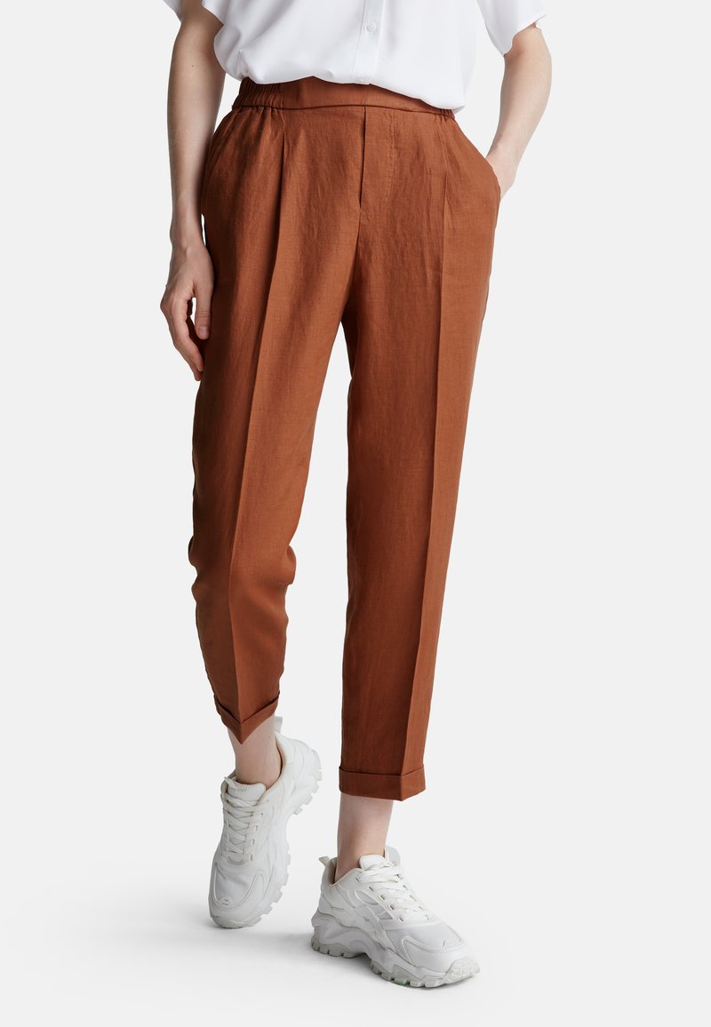 Hnědé, lehké lněné kalhoty s uvolněným střihem, elastickým pasem a bočními kapsami, doplněné o bílé sportovní boty.