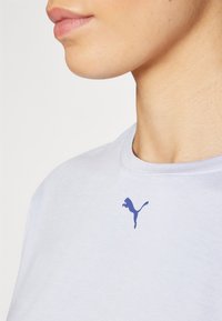 Ljusblå t-shirt i bomull med en liten lila Puma-logga på bröstet, rund halsringning och korta ärmar. Slät textur.
