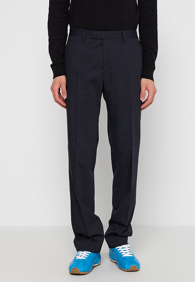 Pantalones de vestir azul marino con un tejido texturizado, corte recto y dos pliegues delanteros, combinados con unas zapatillas deportivas azules y una camiseta negra de manga larga.