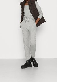 Conjunto de sudadera gris y joggers con cintura ajustable, combinado con un chaleco acolchado sin mangas marrón y botas de tobillo negras. Texturas suaves en todo.