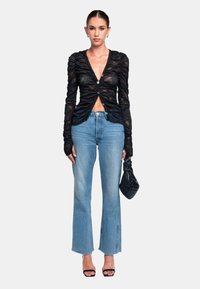 Schwarz durchsichtiges Langarmtop mit Raffung und Knopfverschluss, kombiniert mit hellblauen weit geschnittenen Jeans und einer schwarzen Clutch. Riemchenabsätze.