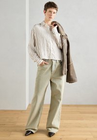 Gaiši svītrota, pogu krekls apakšā ar brīvām, gaiši zaļām džinsām. Tumši brūna ādas jaka uz viena pleca. Norādīti melni papēži.