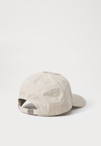 Beige bomull caps med rund krone, buet skjerm og justerbar stropp bak. Har søm og ventilasjonsåpninger.