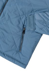 Manche de veste bleue matelassée avec poignet côtelé et une poche zippée verticale près du poignet sur un fond blanc.