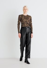 Haut à manches longues en imprimé léopard associé à un pantalon en simili cuir noir taille haute et des bottines à talons noirs. Fond uni.