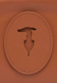 Bruine leren portemonnee met een cirkelvormig uitsparingsontwerp. Glad van textuur met nauwkeurige stiksels rondom de omtrek en een centraal motief.