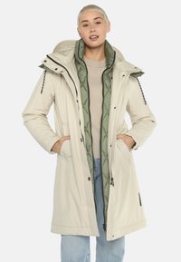 Lichtbeige geïsoleerde jas met een afneembare groene voering, ritssluiting, verstelbare capuchon en zijzakken, ontworpen voor warmte en bedekking.