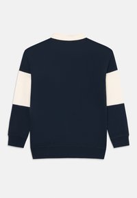 Sötétkék pulóver, krém színű panel részletezéssel az ujjakon. Galléros nyakkal és bordázott mandzsettával és derékkal rendelkezik, hogy illeszkedő megjelenést biztosítson.